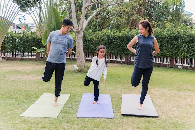 Jeune mère asiatique, père et fille enfant pratiquant l'exercice d'étirement ensemble avant l'entraînement de yoga en plein air le matin dans la nature un parc de jardin sur le terrain. Famille heureuse enfant sport mode de vie sain