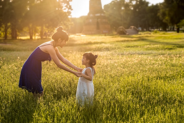 Jeune mère asiatique s'amuser avec sa fille dans le champ avec la lumière du soleil sur l'herbe