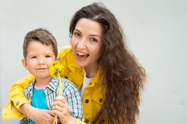 Jeune mère aux cheveux bouclés et un enfant tenant des fleurs.