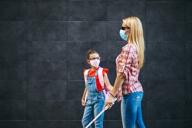 Jeune mère aveugle marchant avec sa petite fille dans la rue de la ville. Ils portent des masques de protection du visage. Retour à l'école et nouveau concept de mode de vie du coronavirus.