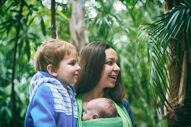 Une jeune mère avec un bébé en écharpe et un petit garçon marche dans la jungle