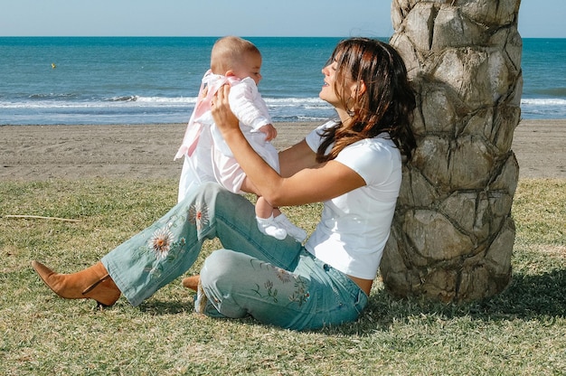 Jeune mère caucasienne assise sur l'herbe avec bébé dans ses bras au bord de la mer