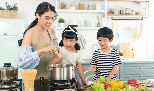 Jeune mère célibataire asiatique faisant de la nourriture tout en prenant soin de son enfant dans la cuisine