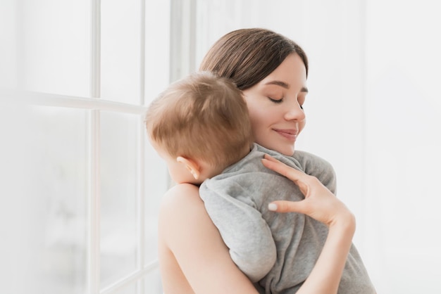 Une jeune mère célibataire berce son petit fils, sa petite fille, son nouveau-né, son bébé, son enfant, sa sieste, son sommeil et son coucher.