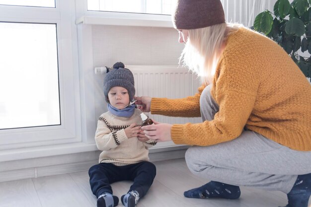 Une jeune mère dans un chandail jaune mesure la température de l'enfant et donne des médicaments pour la maladie