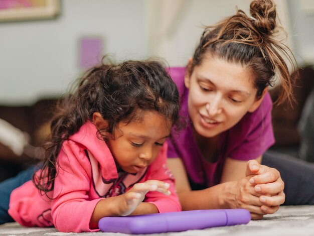 Jeune mère du millénaire et fille d'âge préscolaire diversifiée à la maison se liant à l'aide d'une tablette