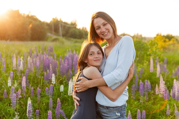 Jeune mère embrassant son enfant femme et adolescente en plein air sur le terrain d'été avec fleurs sauvages f