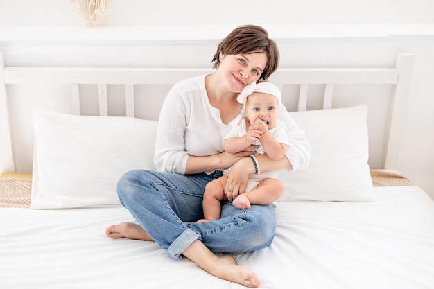 une jeune mère embrasse doucement son enfant en l'embrassant et en l'admirant une mère de famille heureuse et son bébé sur le lit jouant et s'amusant l'amour et les soins maternels une maman heureuse en congé de maternité