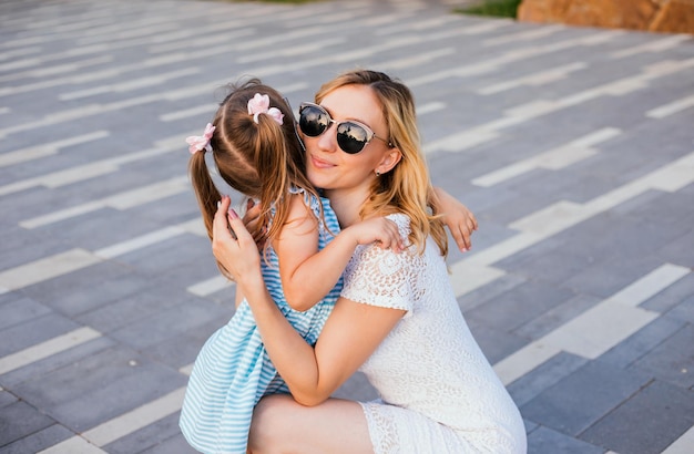 Une jeune mère embrasse sa petite fille dans le parc Une femme à lunettes de soleil