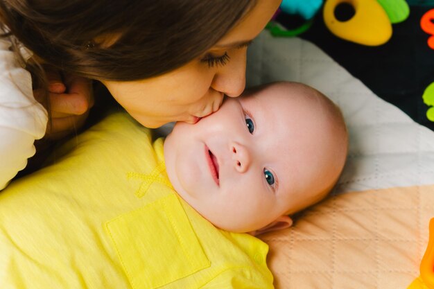 Une jeune mère embrasse son adorable nouveau-né sur la joue à la maison Le concept d'une famille heureuse