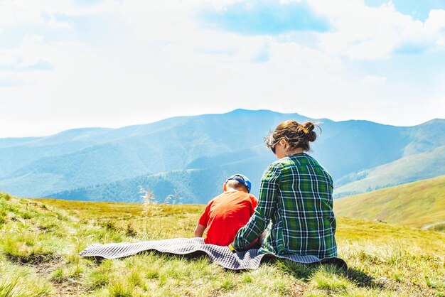 Jeune mère avec enfant assis sur une couverture au sommet de la montagne belle vue sur le paysage sur l'espace de copie de concept de voyage en arrière-plan