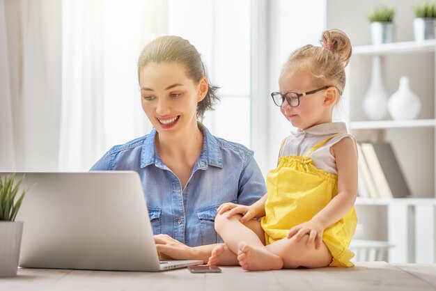 Jeune mère avec enfant en bas âge travaillant sur l'ordinateur à la maison.