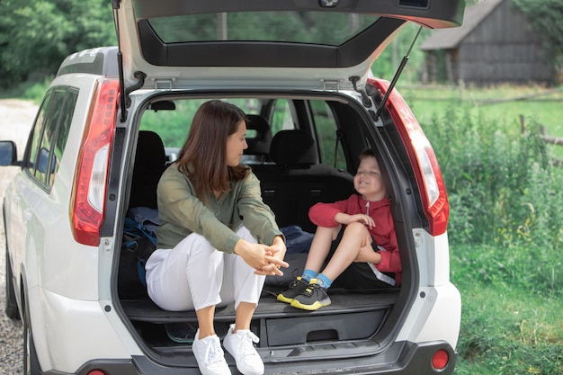 Jeune mère avec enfant garçon assis dans le coffre de la voiture se reposant dans le concept de voyage sur la route journée ensoleillée d'été