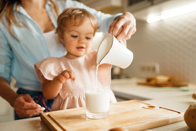 Jeune mère et enfant verse du lait dans un verre, ingrédients pour la pâtisserie