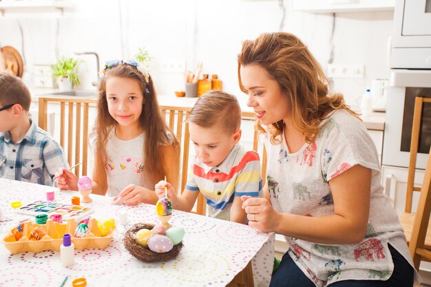 Jeune mère et enfants joyeux peignant des œufs colorés. Maman, enfant d'âge préscolaire et écolière décorent les oeufs de Pâques.