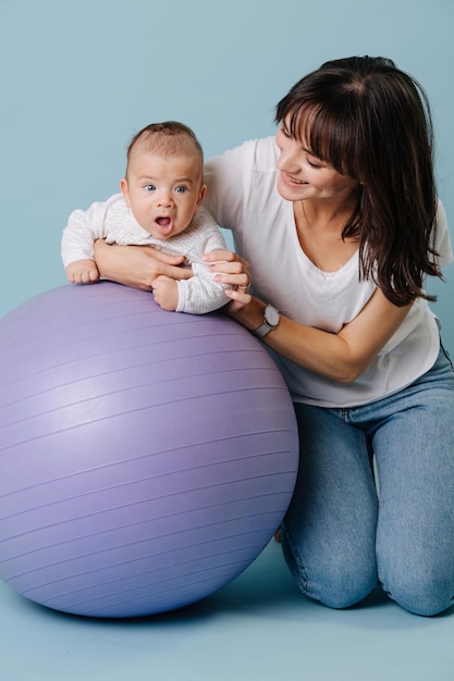 Jeune mère est engagée dans des exercices avec son bébé, sur un ballon de fitness, image sur fond bleu