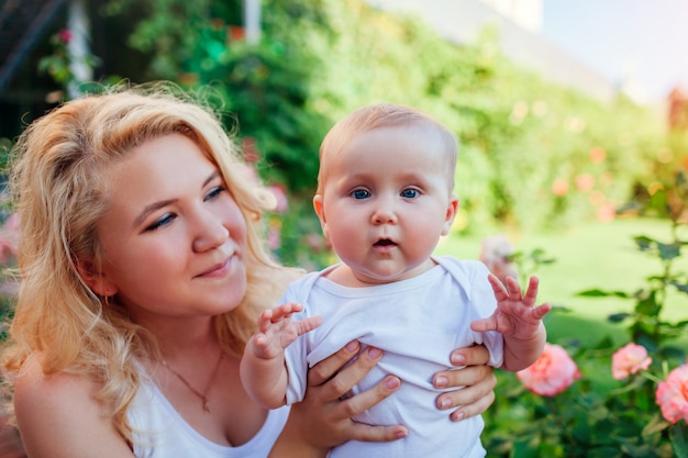 Jeune mère étreignant bébé RIF dans le jardin de roses. Enfant regardant la caméra.