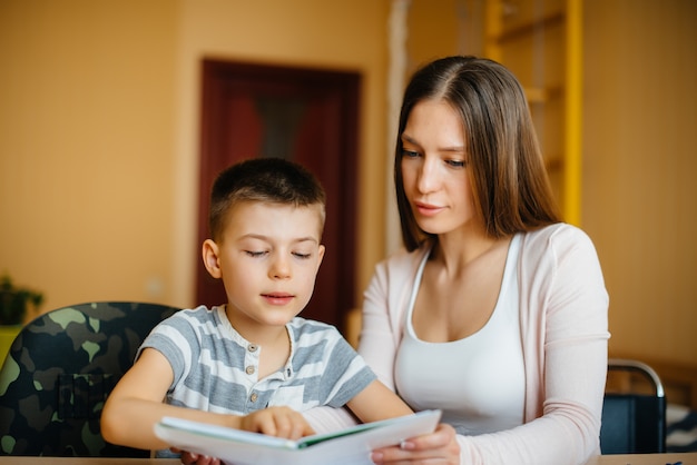 Une jeune mère fait ses devoirs avec son fils à la maison. Parents et formation