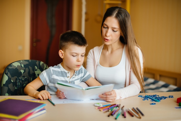 Une jeune mère fait ses devoirs avec son fils à la maison. Parents et formation