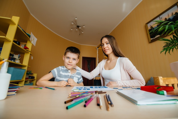 Une jeune mère fait ses devoirs avec son fils à la maison. Parents et formation