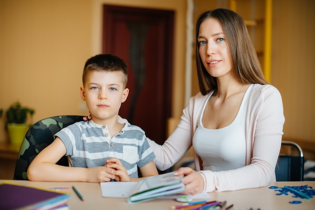 Une jeune mère fait ses devoirs avec son fils à la maison. Parents et formation