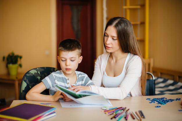 Une jeune mère fait ses devoirs avec son fils à la maison. Parents et formation