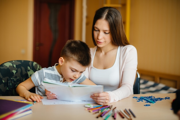 Une jeune mère fait ses devoirs avec son fils à la maison. Parents et formation.