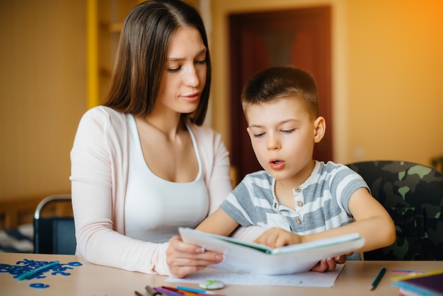 Une jeune mère fait ses devoirs avec son fils à la maison. Parents et formation.