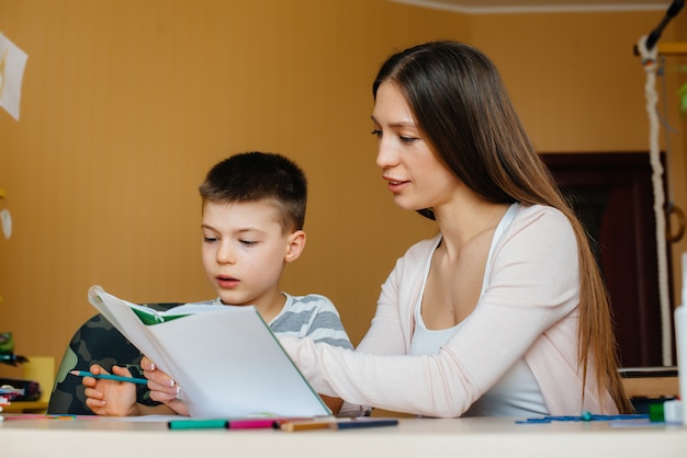 Une jeune mère fait ses devoirs avec son fils à la maison. Parents et formation.
