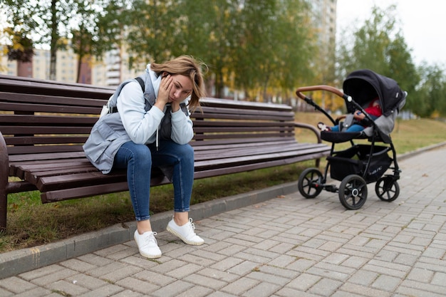 Une jeune mère fatiguée avec son petit fils dans une poussette s'endort sur un banc dans le parc