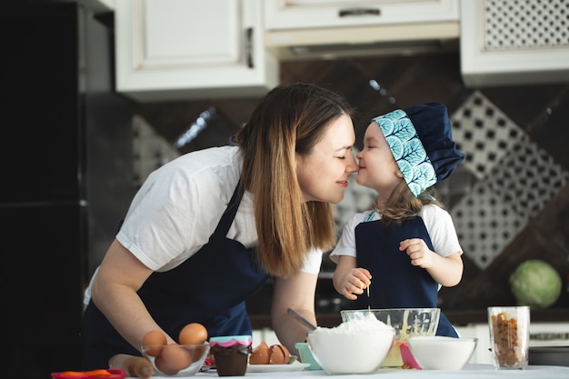 Jeune mère et fille dans la cuisine préparant des cupcakes et la jeune fille embrasse sa mère.