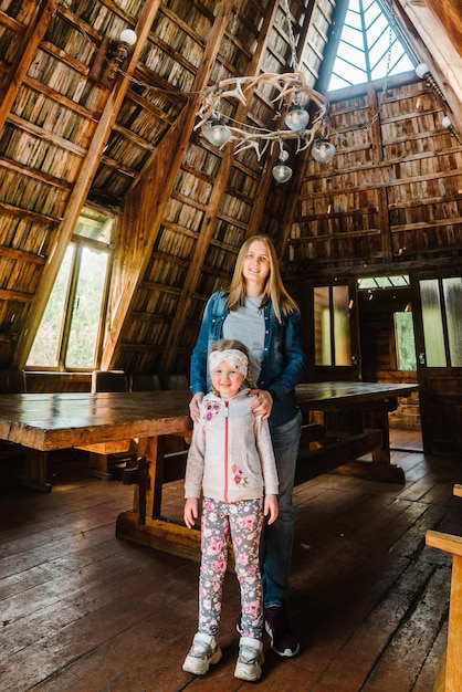 Jeune mère et fille debout dans une vieille maison en bois Heureuse mère étreint la fille Vieille maison architecturale en bois