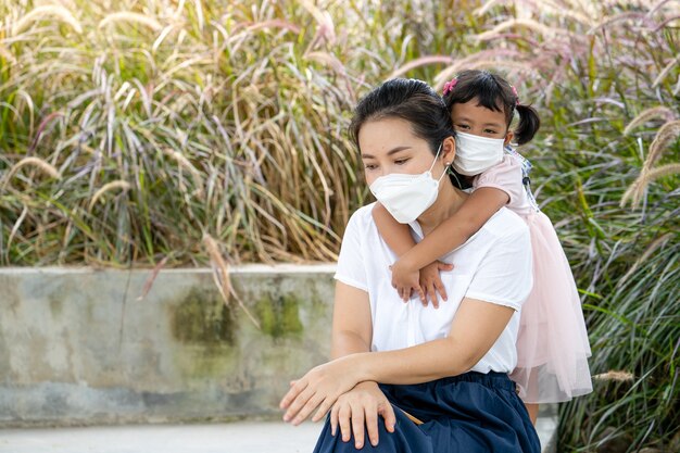 jeune mère et fille avec masque protecteur assis au parc