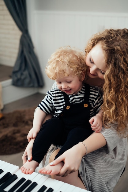 Une jeune mère frisée apprend à son petit fils à jouer du piano en riant