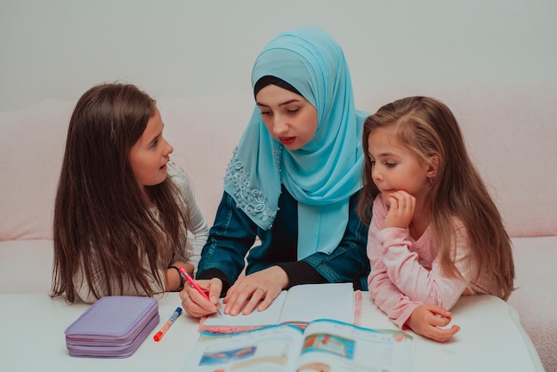 Jeune mère en hijab enseignant sa fille à l'école musulmane à la maison