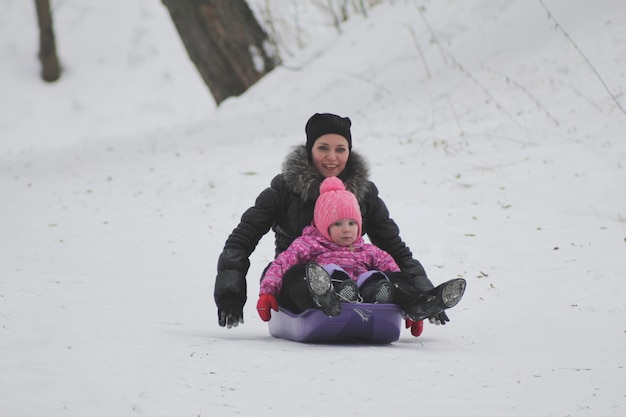 Jeune mère et jolie fille à cheval sur un traîneau dans le parc d'hiver