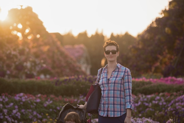 jeune mère et jolie petite fille dans une poussette de bébé profitant d'une belle journée dans le jardin fleuri