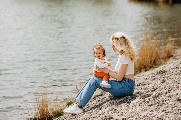 Jeune mère jouant avec sa fille à l'extérieur assise au bord du lac