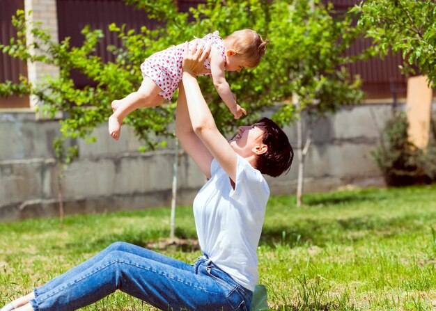 Jeune mère joue avec son bébé sur l'herbe dans le parc. Maman et bébé