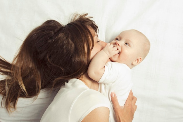 Jeune mère joue avec son bébé sur un lit avec un drap blanc Vue de dessus à plat