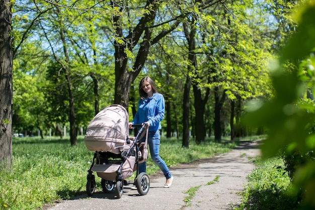 Jeune mère marchant et poussant une poussette dans le parc