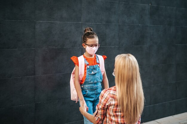 Jeune mère marchant avec sa petite fille dans la rue de la ville. Ils portent des masques de protection du visage. Retour à l'école et nouveau concept de mode de vie du coronavirus.