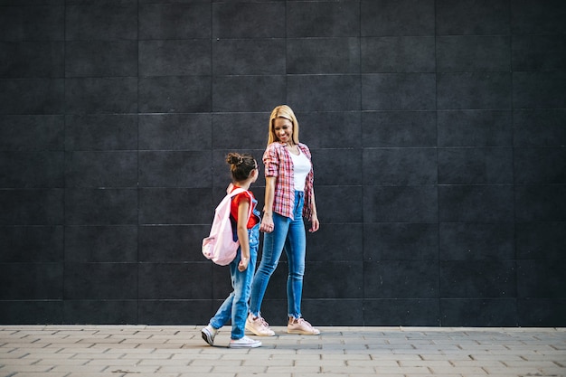 Jeune mère marchant avec sa petite fille à l'école primaire. Retour au concept de l'école.