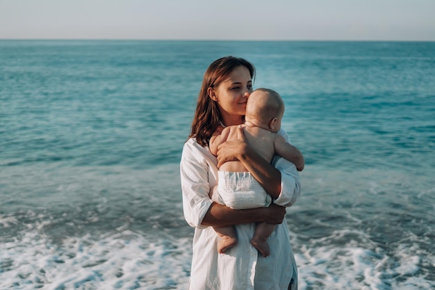 Une jeune mère marche le long de la plage avec un petit enfant en couches