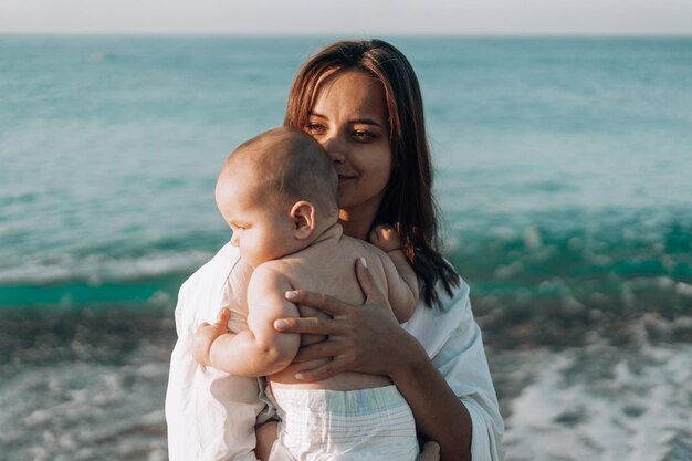 Une jeune mère marche le long de la plage avec un petit enfant en couches