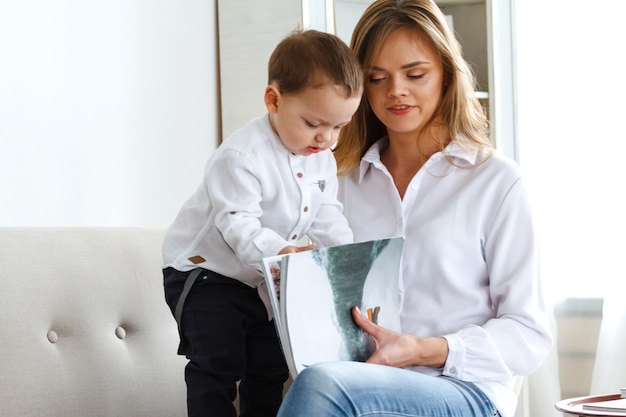 Une jeune mère avec un mignon petit fils lisant un magazine dans un salon confortable et lumineux