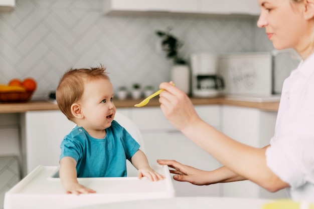 Une jeune mère nourrit son jeune fils qui est assis dans une chaise haute pour nourrir un bébé.