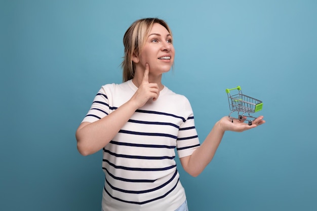 Jeune mère pensant à faire du shopping tenant un panier d'épicerie dans ses mains sur un fond bleu avec