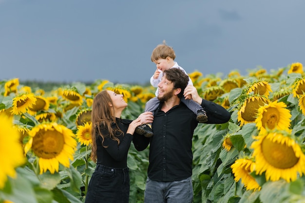 Une jeune mère et un père avec leur jeune fils marchant dans un champ de tournesols un jour d'été
