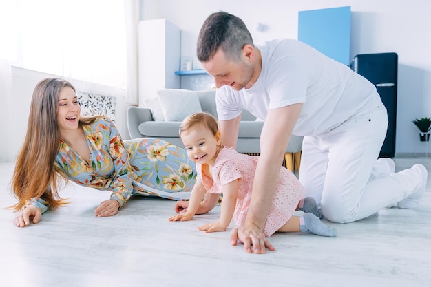 Une jeune mère et un père souriants sont assis par terre dans leur salon à la maison mignonne petite fille rampante près d'eux